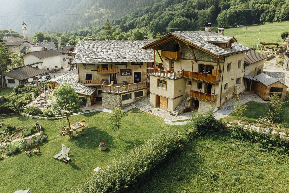 Nella foto si vedono due caseggiati con tetti in losa e balconi in legno, sotto un grande prato verde.