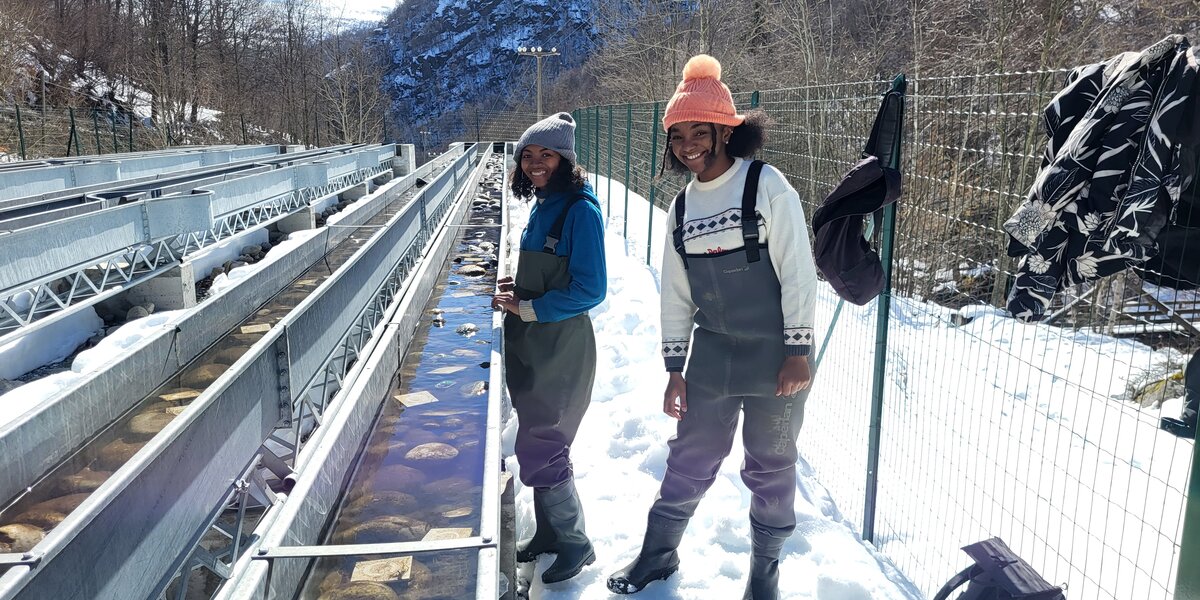 le due ricercatrici in piedi a fianco dei fiumi artificiali del Centro Alpstream: indossano abbigliamento invernale e sul terreno c'è una totale copertura di neve