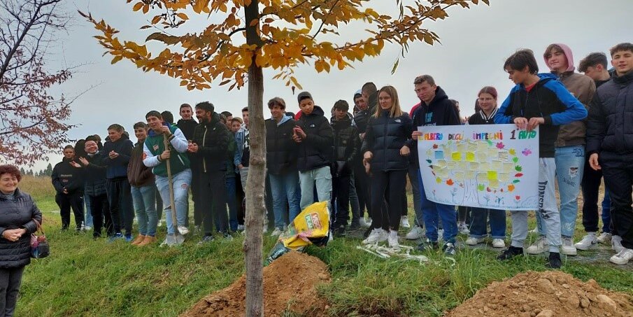 gruppo di studenti dietro a un albero di nuova piantumazione: si vede lo scavo fatto per metterlo a dimora in primo piano.