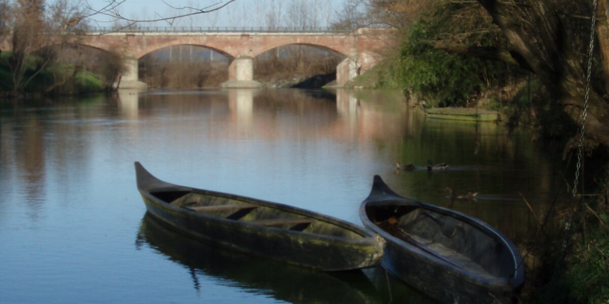 il fiume Po a Villafranca Piemonte con due tipiche imbarcazioni fluviali in primo piano e un ponte sullo sfondo.