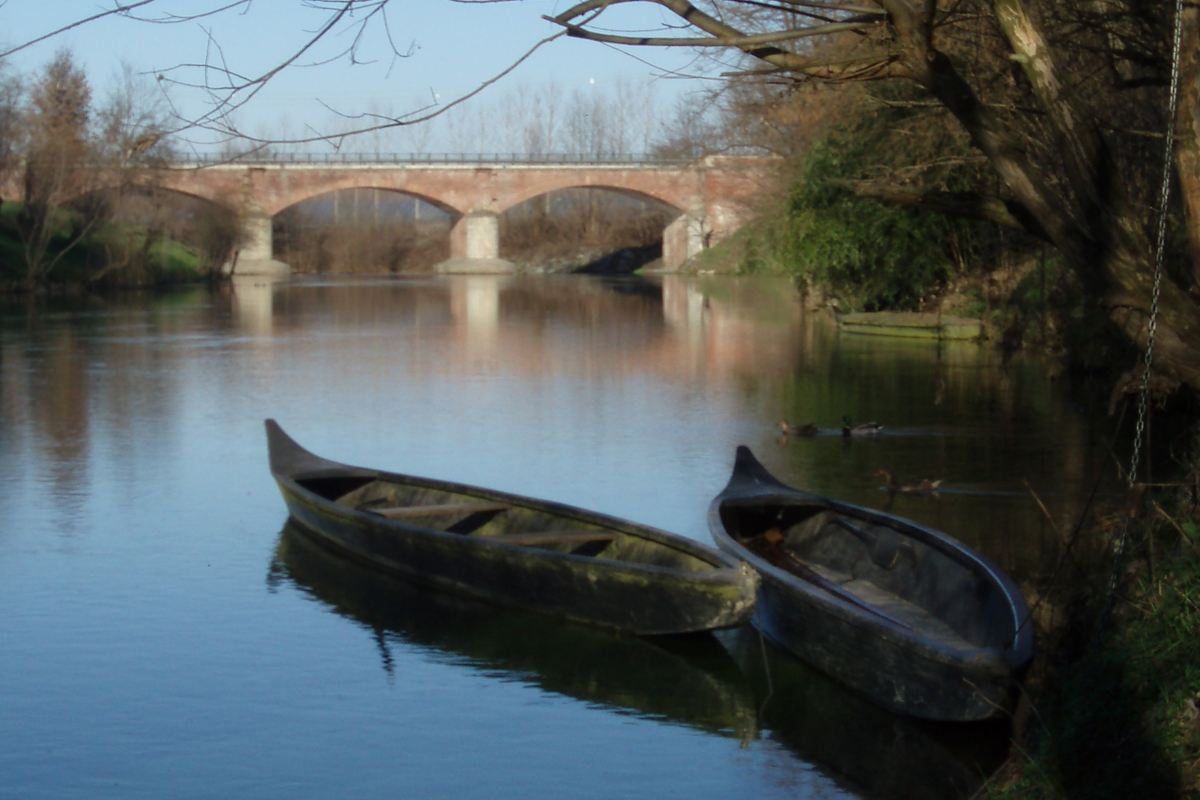 il fiume Po a Villafranca Piemonte con due tipiche imbarcazioni fluviali in primo piano e un ponte sullo sfondo.