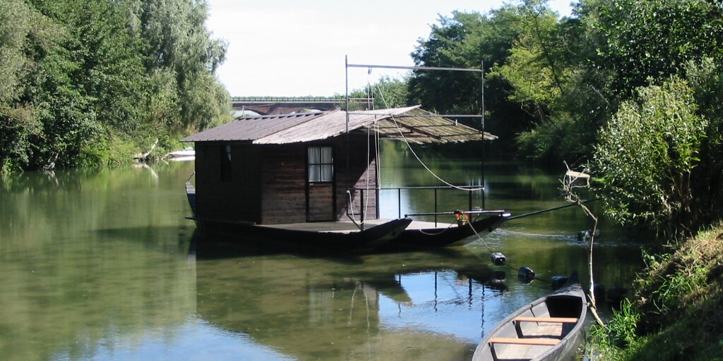 Foto dell'attuale traghetto del Po, attraccato all'approdo. Sullo sfondo il ponte carrabile sul fiume.