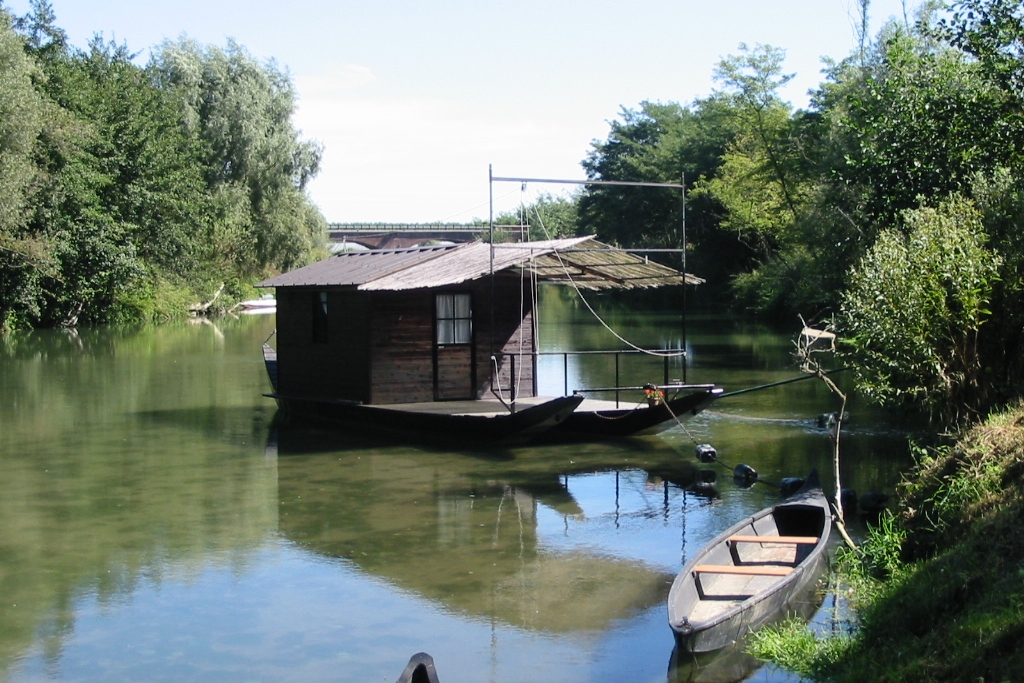 Foto dell'attuale traghetto del Po, attraccato all'approdo. Sullo sfondo il ponte carrabile sul fiume.