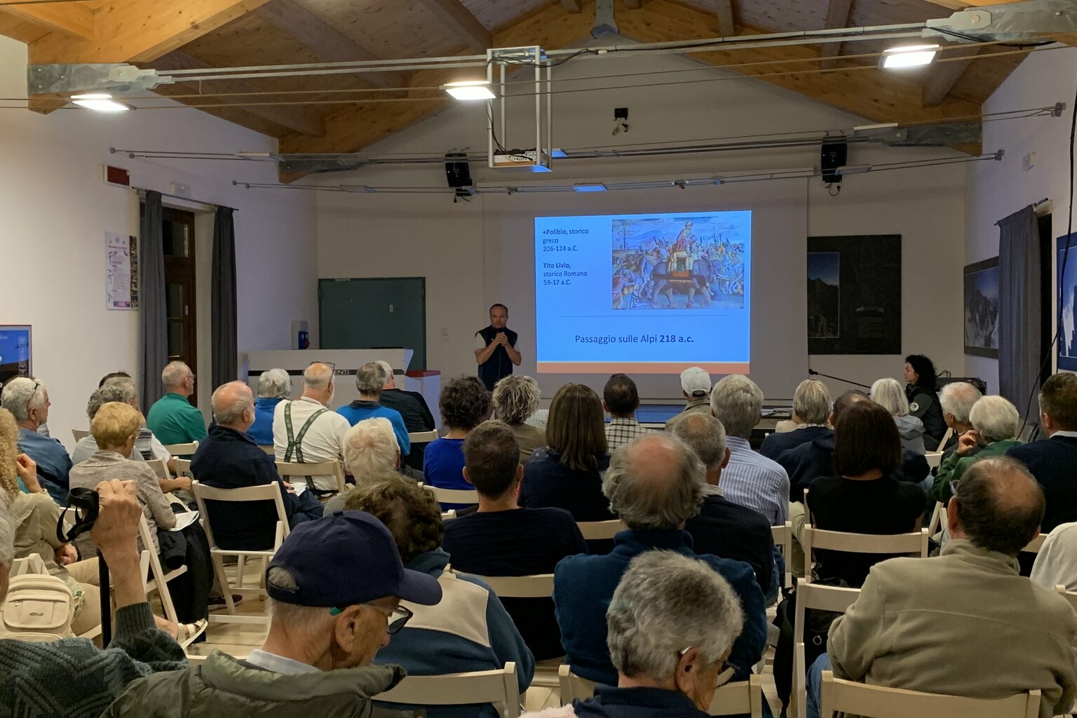 sala piena di persone che ascoltano un funzionario del Parco del Monviso impegnato in una conferenza