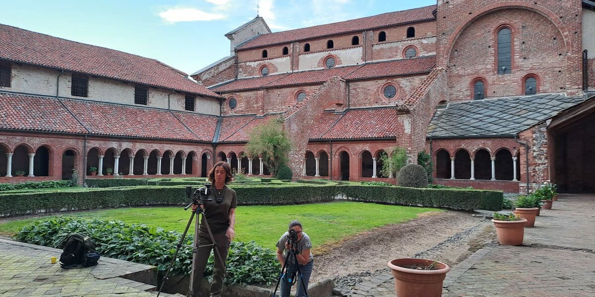 foto scattata nel chiostro dell'Abbazia di Staffarda: in primo piano due donne nei pressi di macchine fotografiche con termocamera, sullo sfondo l'architettura del complesso monastico