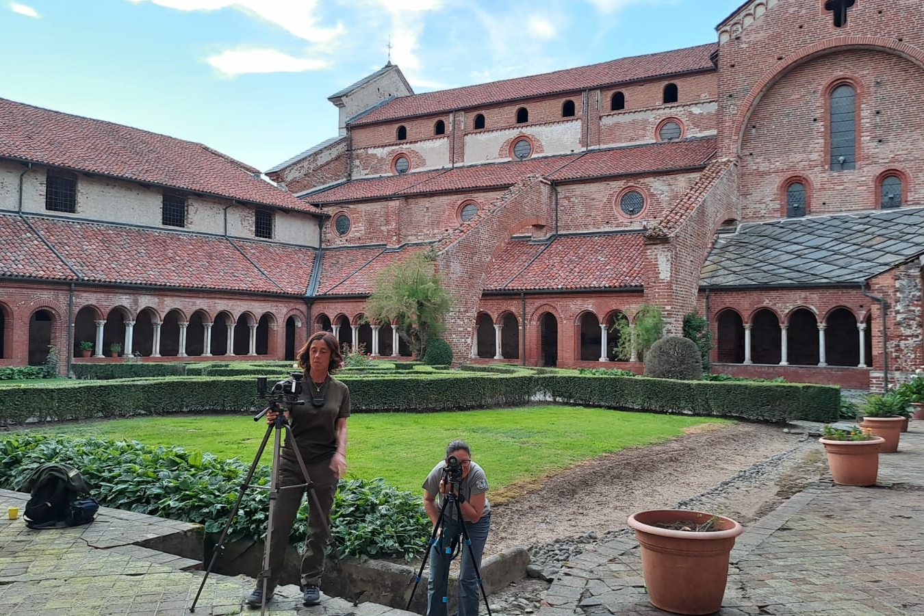 foto scattata nel chiostro dell'Abbazia di Staffarda: in primo piano due donne nei pressi di macchine fotografiche con termocamera, sullo sfondo l'architettura del complesso monastico