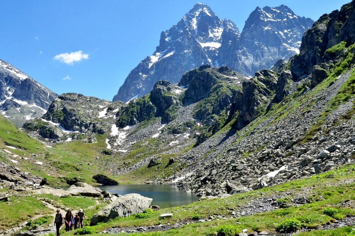 escursionisti camminano nei pressi di un lago: sullo sfondo a destra il Monviso con un cielo azzurro