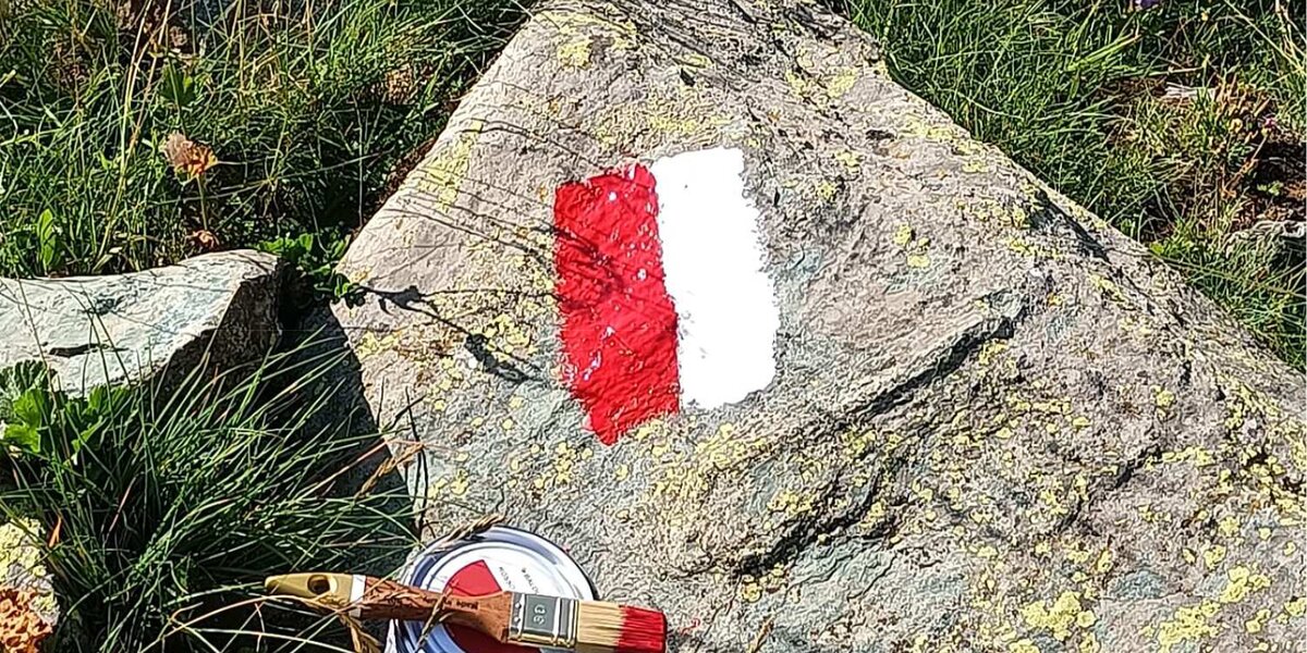 una tacca segnavia in vernice bianca e rossa su una roccia, a lato il pennello e la vernice usata per ridipingere la traccia