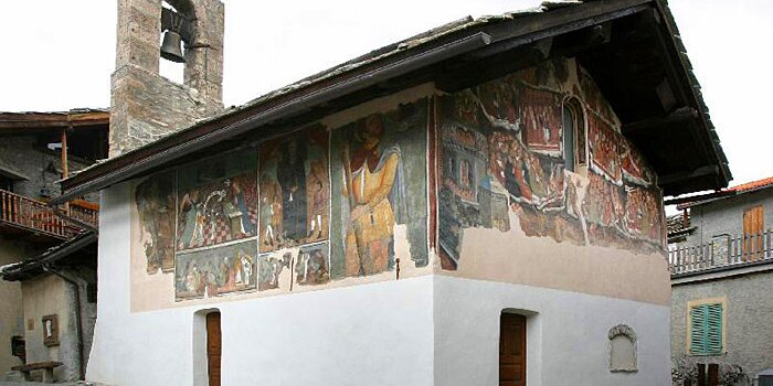 Esterno di un edificio religioso con numerose decorazioni pittoriche sulle pareti e un campaniletto a vela