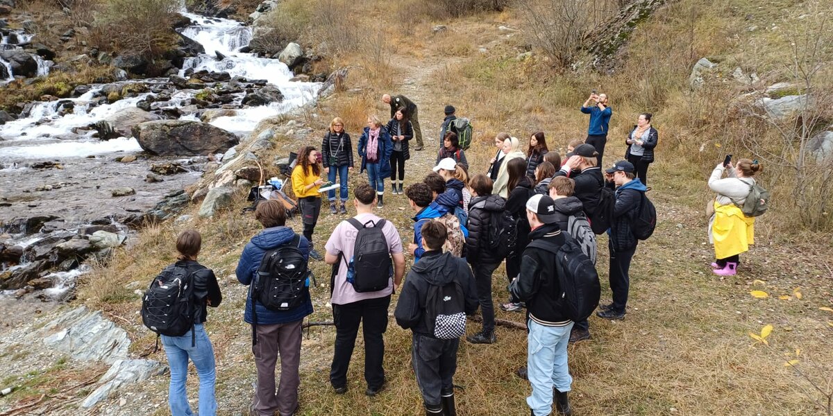 gruppo di studenti all'aperto, in un contesto autunnale. Giornata nuvolosa, sulla sinistra della foto un corso d'acqua montano.
