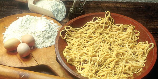 i preparati per fare la pasta: a sinistra uova, olio e farina, a destra i tajarin in un piatto