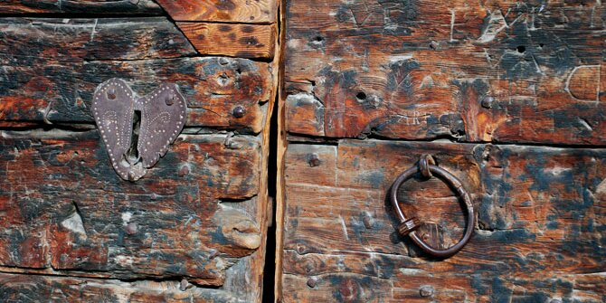 Dettaglio architettonico di un edificio a Chianale, frazione di Pontechianale: si vede una porta di legno con serratura e batacchio.