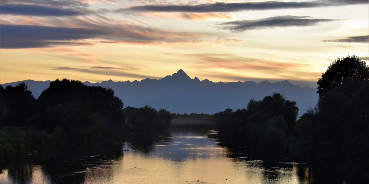 Il Monviso visto al tramonto da un ponte sul fiume Po: l'immagine è dominata dai toni del blu.