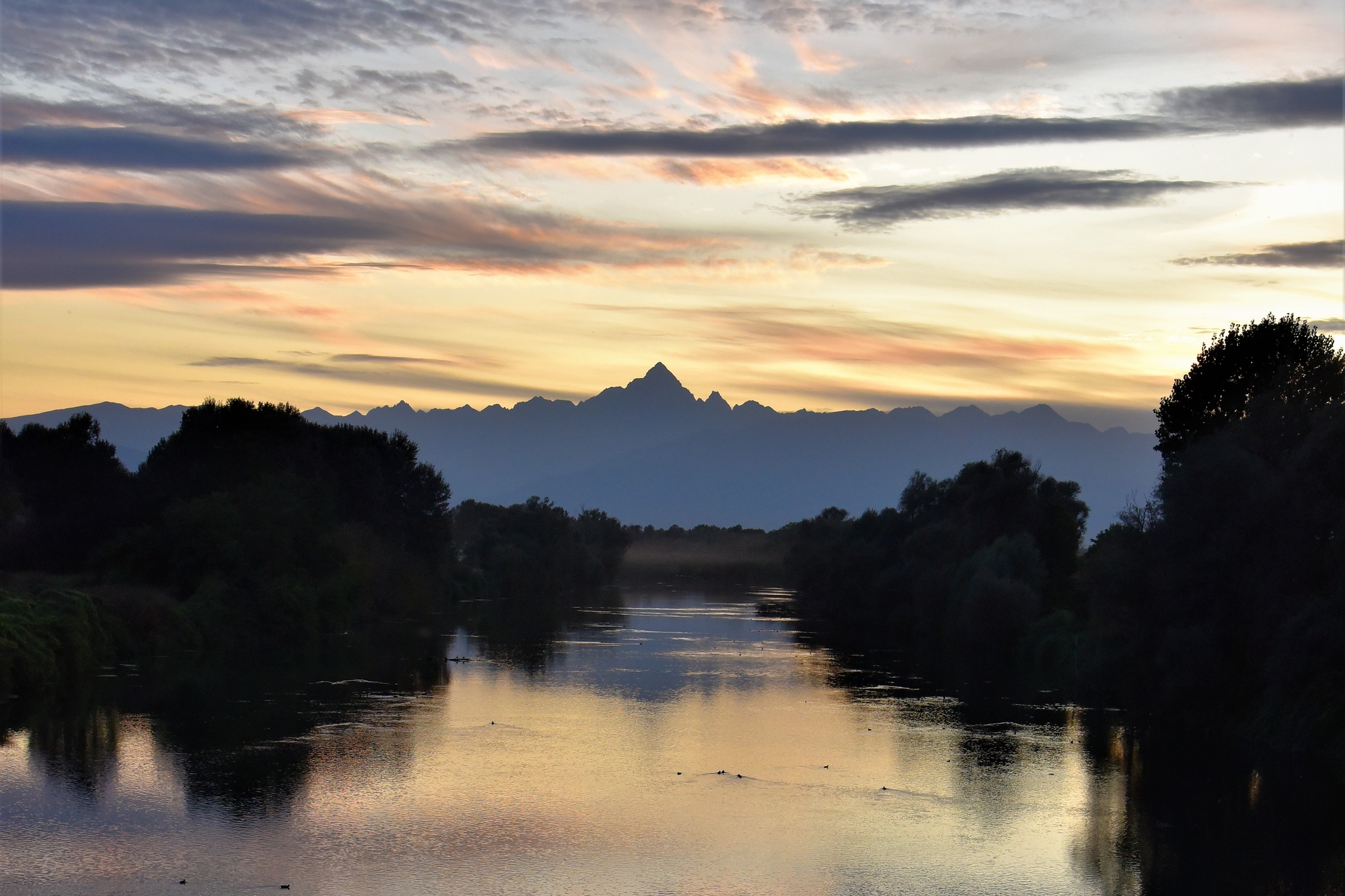 Il Monviso visto al tramonto da un ponte sul fiume Po: l'immagine è dominata dai toni del blu.