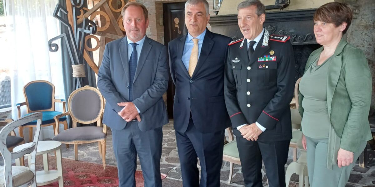 quattro persone a figura intera ritratte in un interno: tre uomini, di cui uno indossa la divisa dei Carabinieri, e una donna.