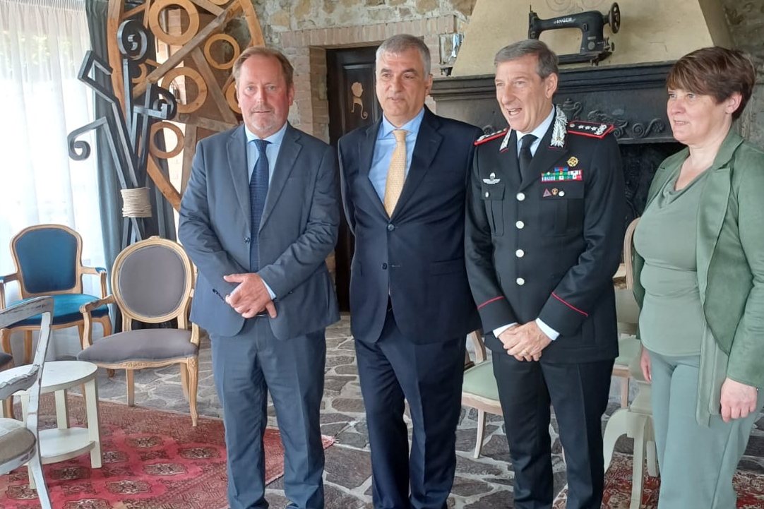 quattro persone a figura intera ritratte in un interno: tre uomini, di cui uno indossa la divisa dei Carabinieri, e una donna.