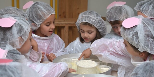 bambini con camici e cuffiette manipolano del formaggio