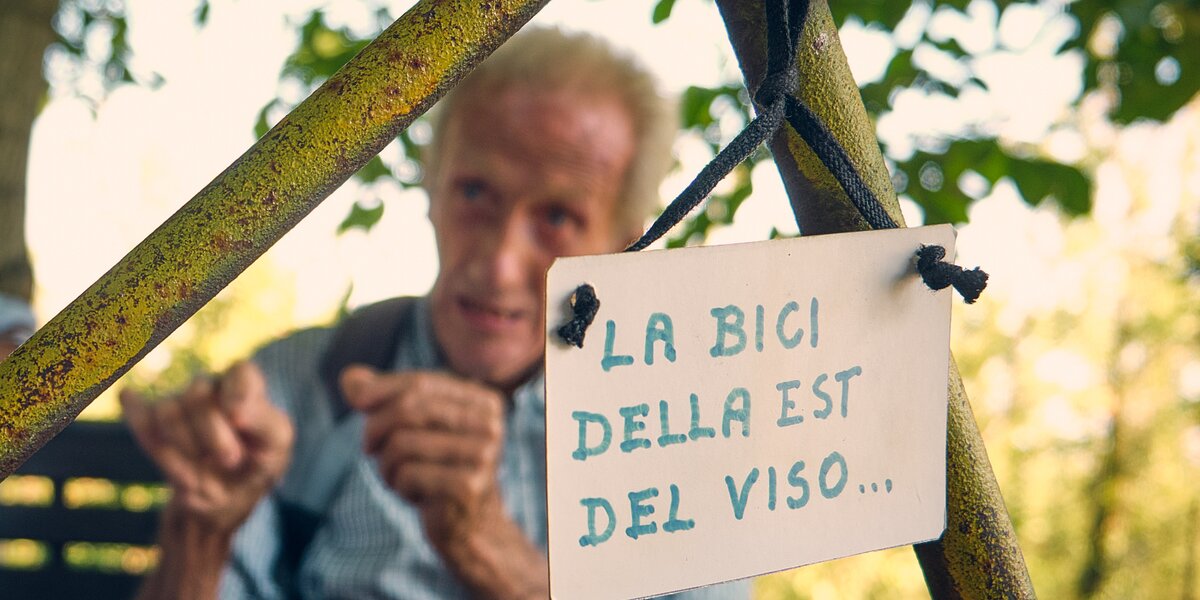 In primo piano si vede una parte del telaio della bicicletta, con un cartellino appeso su cui si legge la bici della Est del Viso...; in secondo piano e sfocato c'è Clemente Berardo.