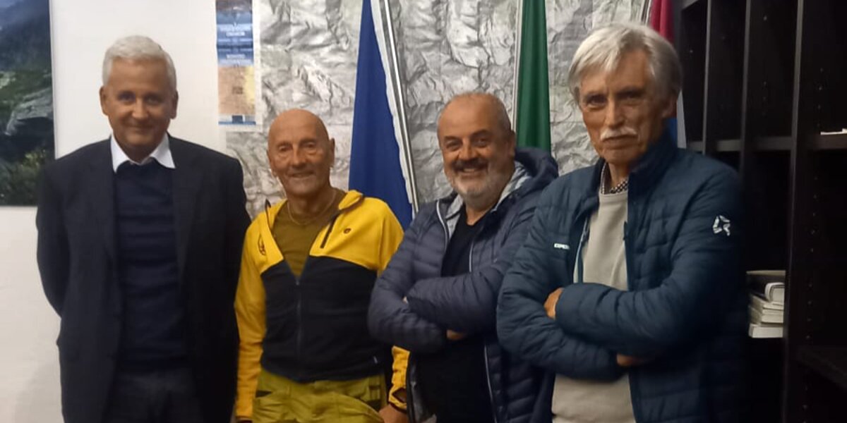 quattro uomini in piedi davanti a una parete con una carta topografica e bandiere.