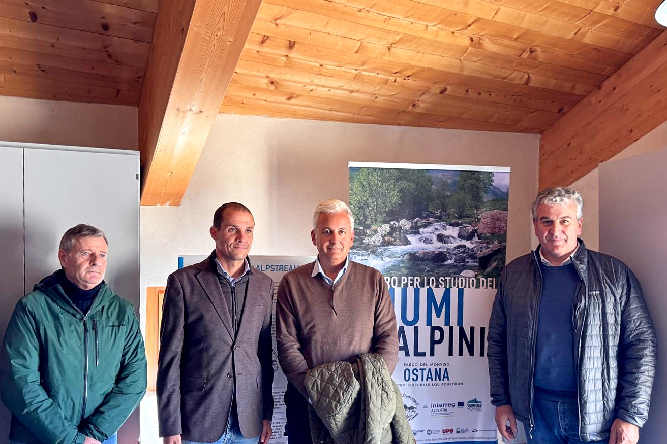 quattro uomini in un ambiente interno con travatura in legno a vista. Si vede un roll up con il logo del Centro per lo Studio dei Fiumi Alpini - ALPSTREAM.
