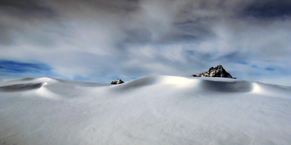 La punta del Monviso e quella della Cima delle Lobbie spuntano in secondo piano da un rilievo innevato in primo piano.