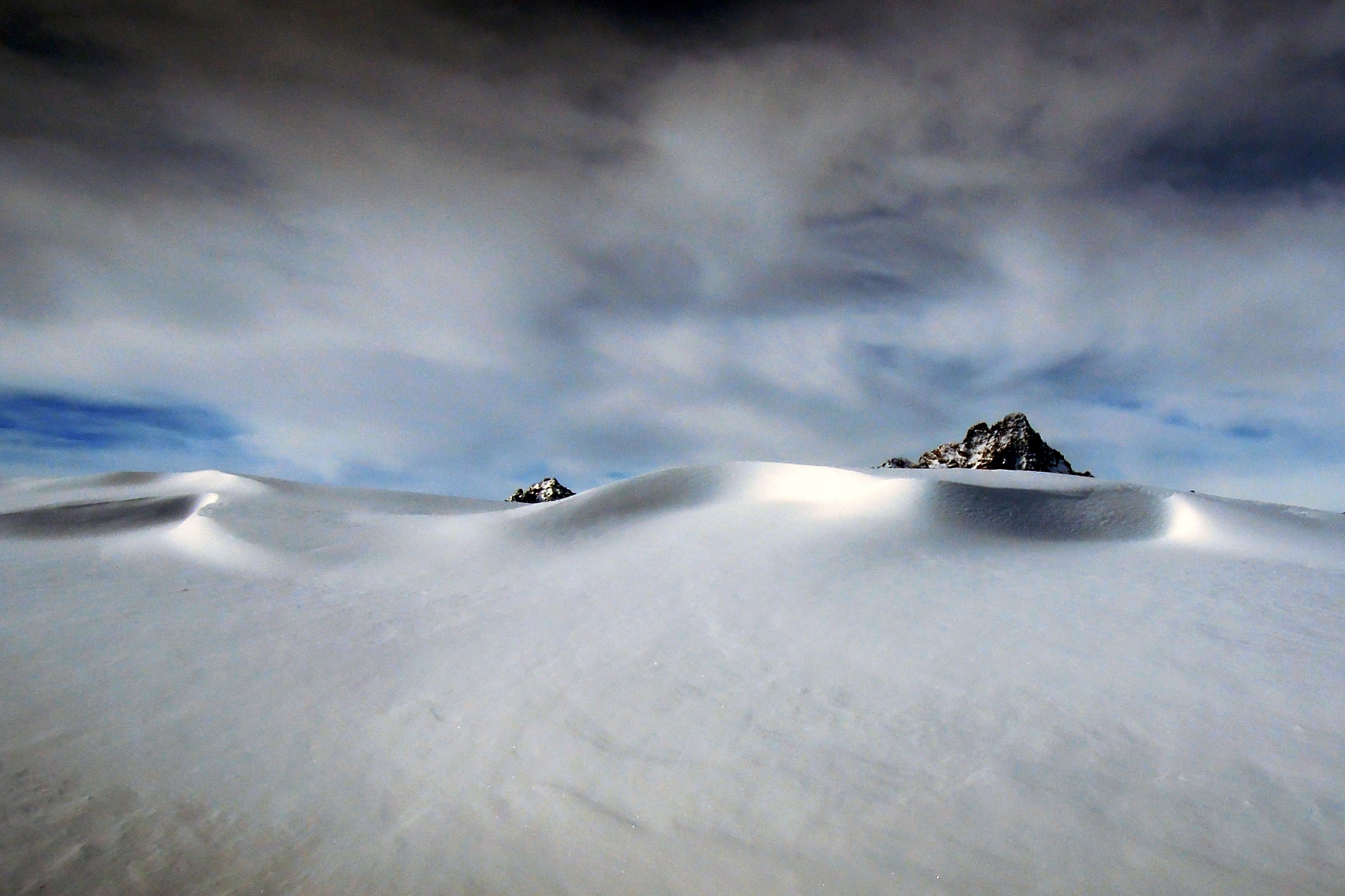 La punta del Monviso e quella della Cima delle Lobbie spuntano in secondo piano da un rilievo innevato in primo piano.