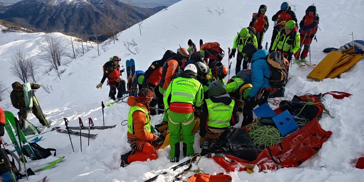 Esercitazione di recupero travolti da valanga: un gruppo di persone su un pendio alpino innevato simula la ricerca di persone nella neve.
