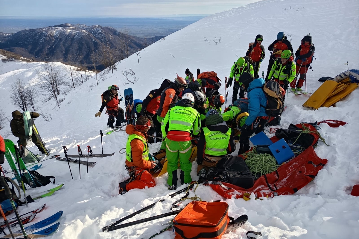 Esercitazione di recupero travolti da valanga: un gruppo di persone su un pendio alpino innevato simula la ricerca di persone nella neve.