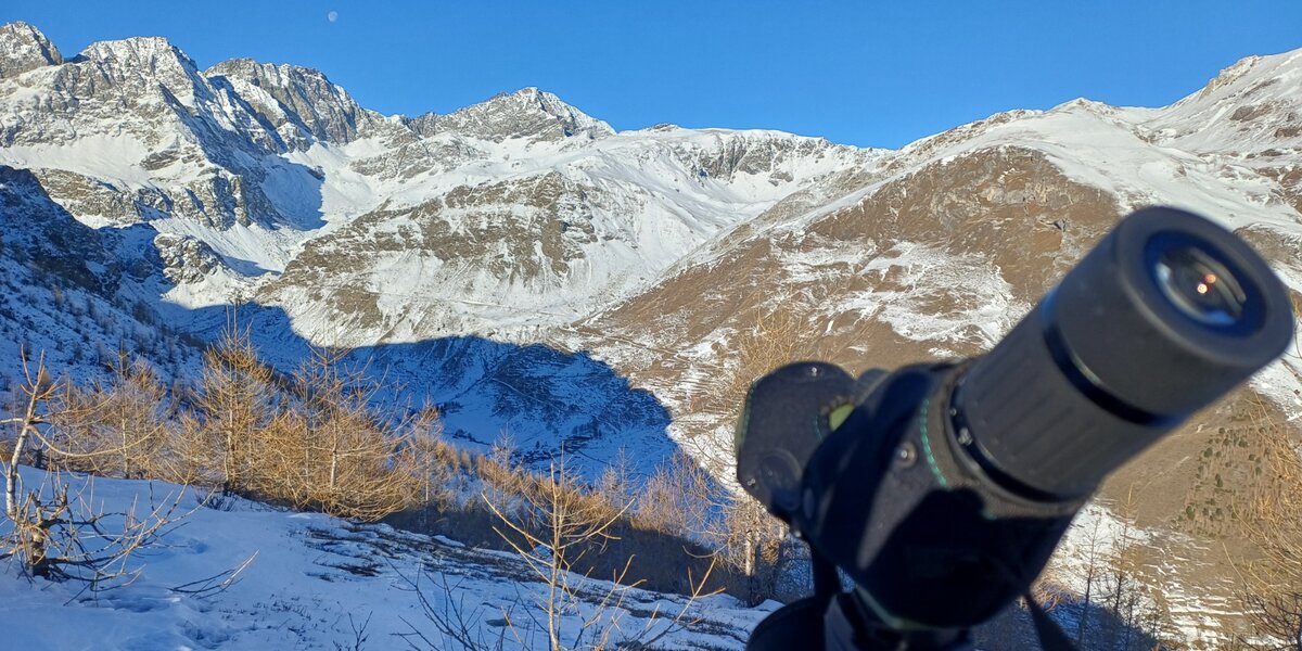 un cannocchiale in primo piano e rivolto verso l'arco alpino. Zona di montagna innevata sullo sfondo.
