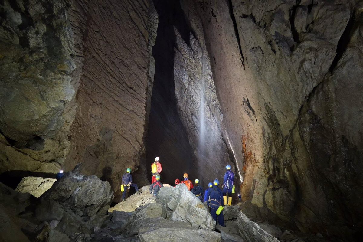 Gruppo di visitatori con caschi e luci frontali all'interno di un'alta grotta di pietra, mentre osservano una cascata sotterranea.