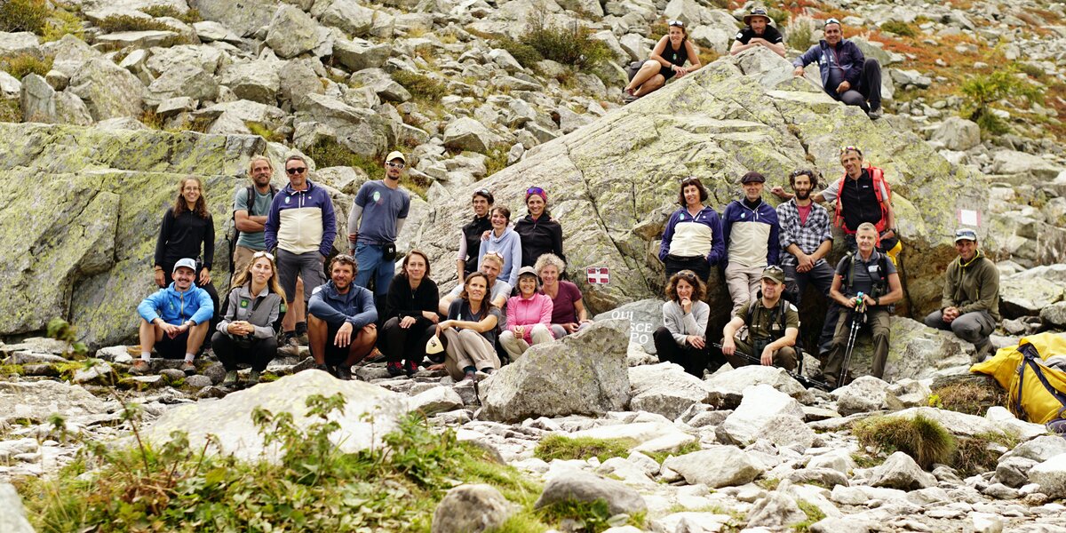 foto di gruppo alle sorgenti del Po: uomini e donne in abbigliamento da montagna posti ai due lati della pietra che indica il luogo dove nasce il Po.