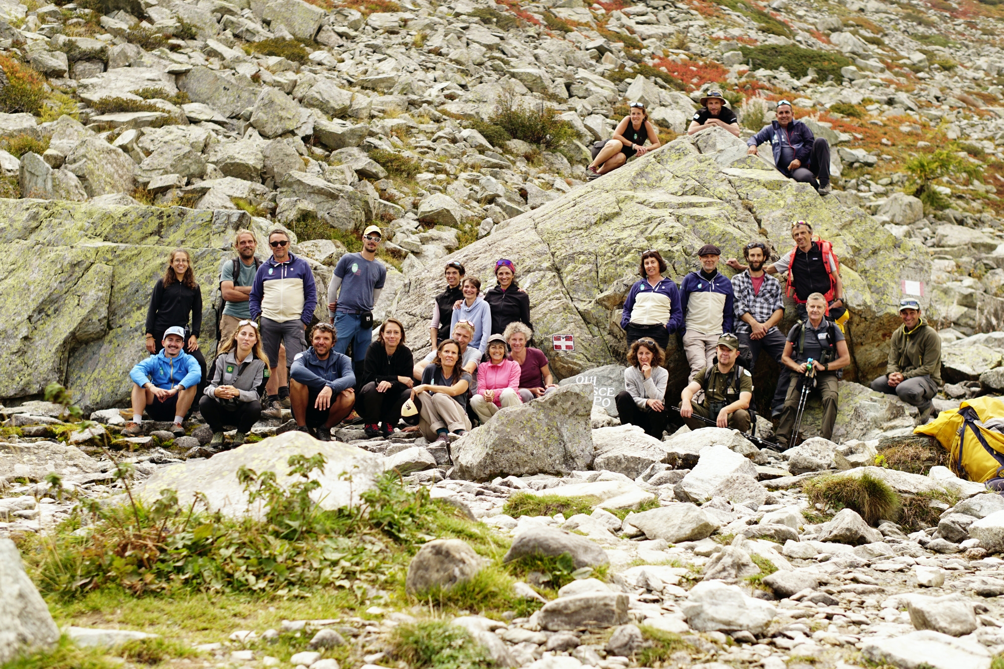 foto di gruppo alle sorgenti del Po: uomini e donne in abbigliamento da montagna posti ai due lati della pietra che indica il luogo dove nasce il Po.