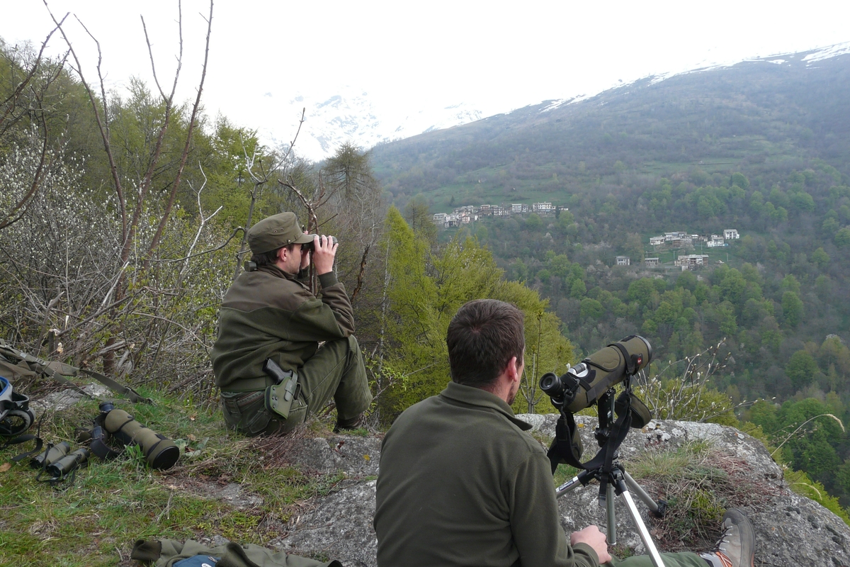 Due guardiaparco in cima a un promontorio montano osservano l'orizzonte con binocoli