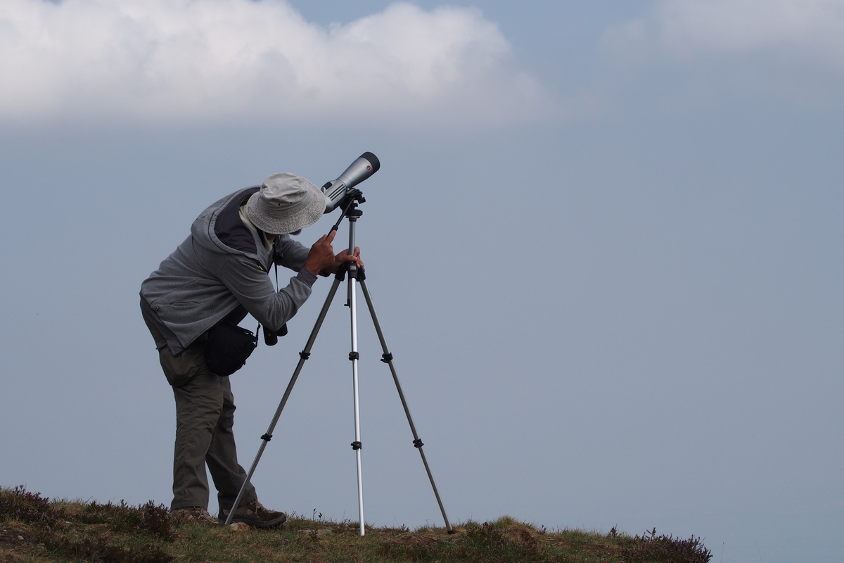 Un uomo in cima a Bric Lumbatera, con un cappello in testa, osserva il cielo con un cannocchiale poggiato su un treppiede.