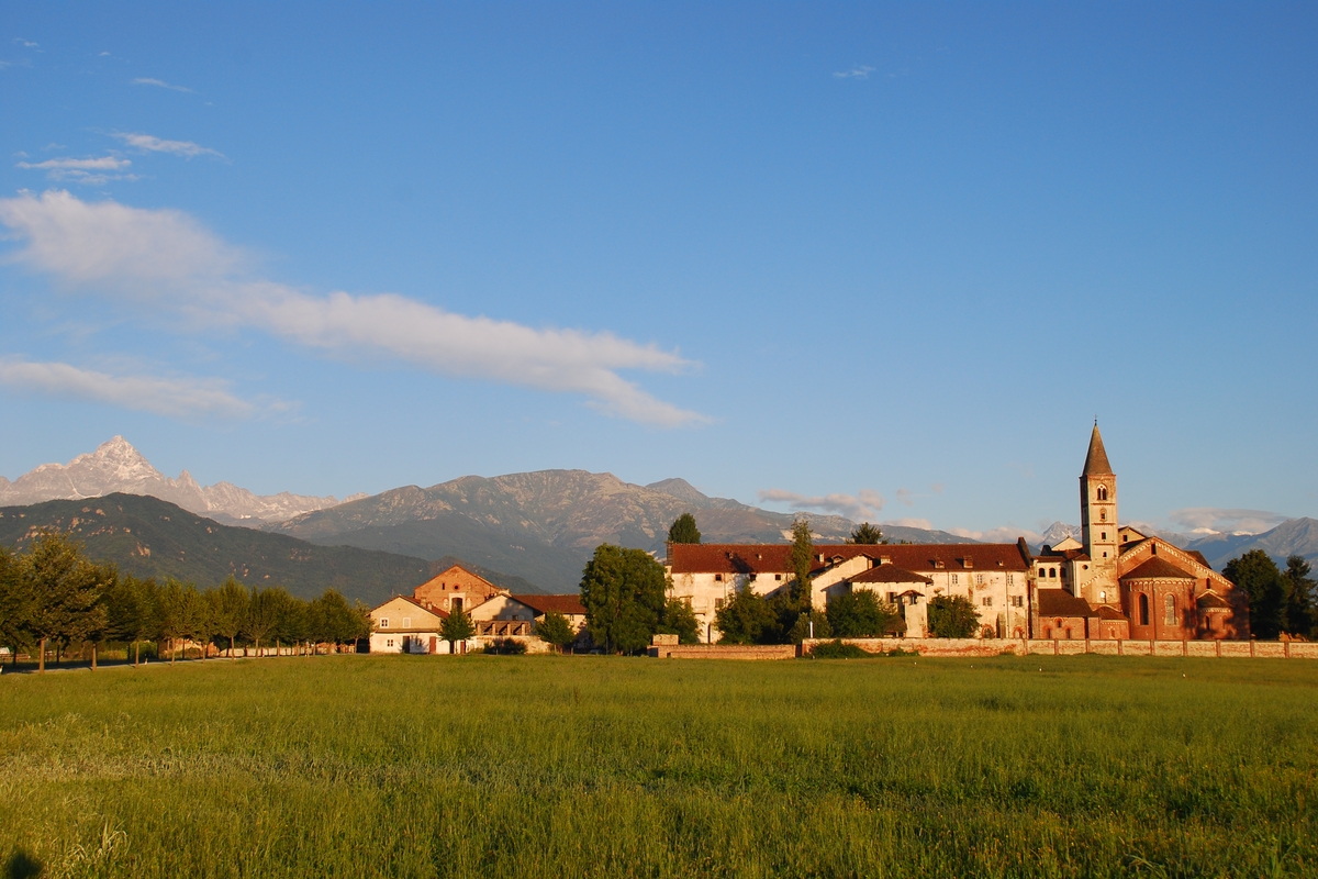 sulla destra in basso il profilo dell'Abbazia di Staffarda, con i numerosi edifici pertinenziali che si sviluppano alla sinistra della struttura religiosa; sullo sfondo a sinistra la silhouette del Monviso