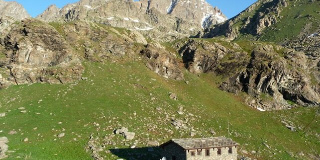 il rifugio alpetto, in pietra immerso nel verde della conca erbosa che lo ospita, sullo sfondo si ergono montagne roccioso