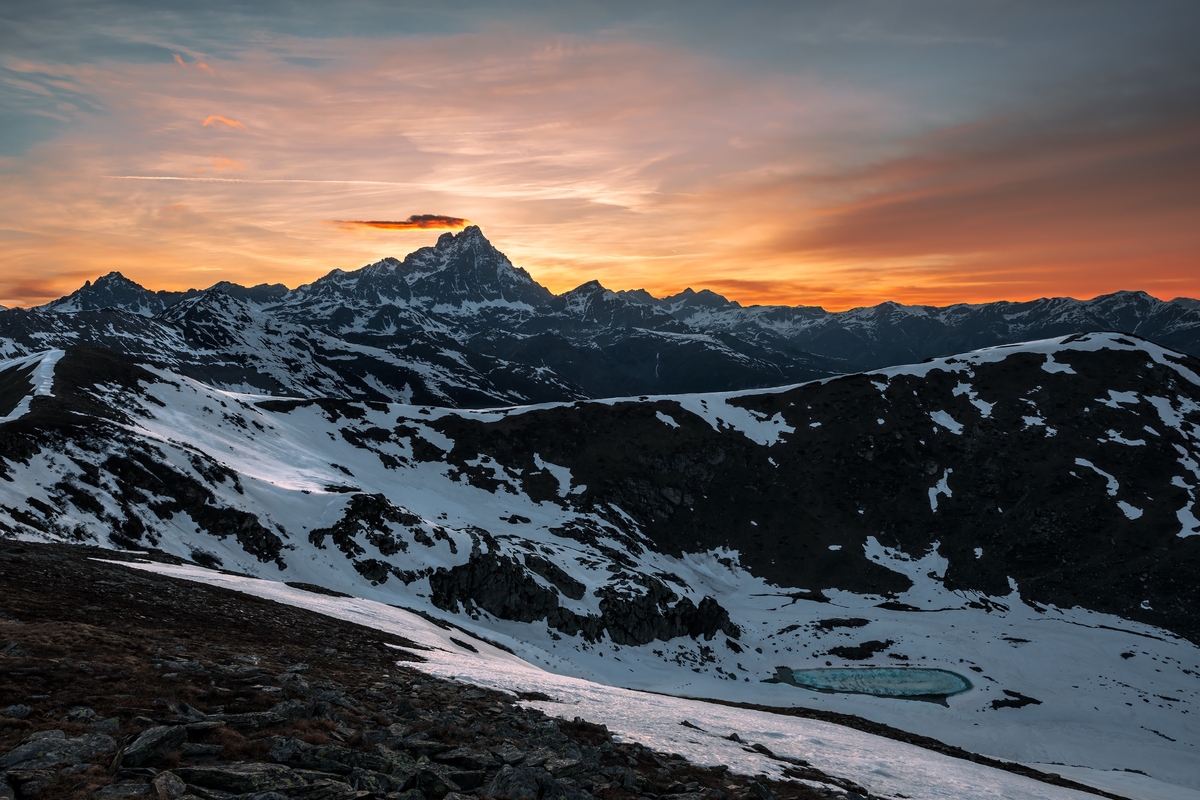 immagine del monviso al tramonto, in primo piano un ambiente montano parzialmente innevato, sullo sfondo il profilo del monviso su un cielo rosa e azzurro